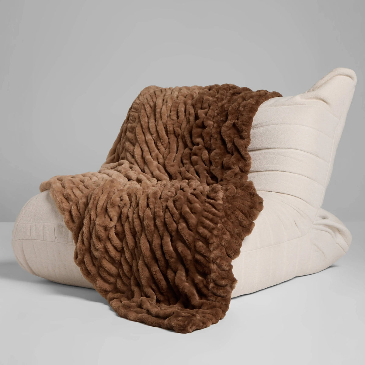 Brown Dreamer plush blanket draped over a cream lounge chair
